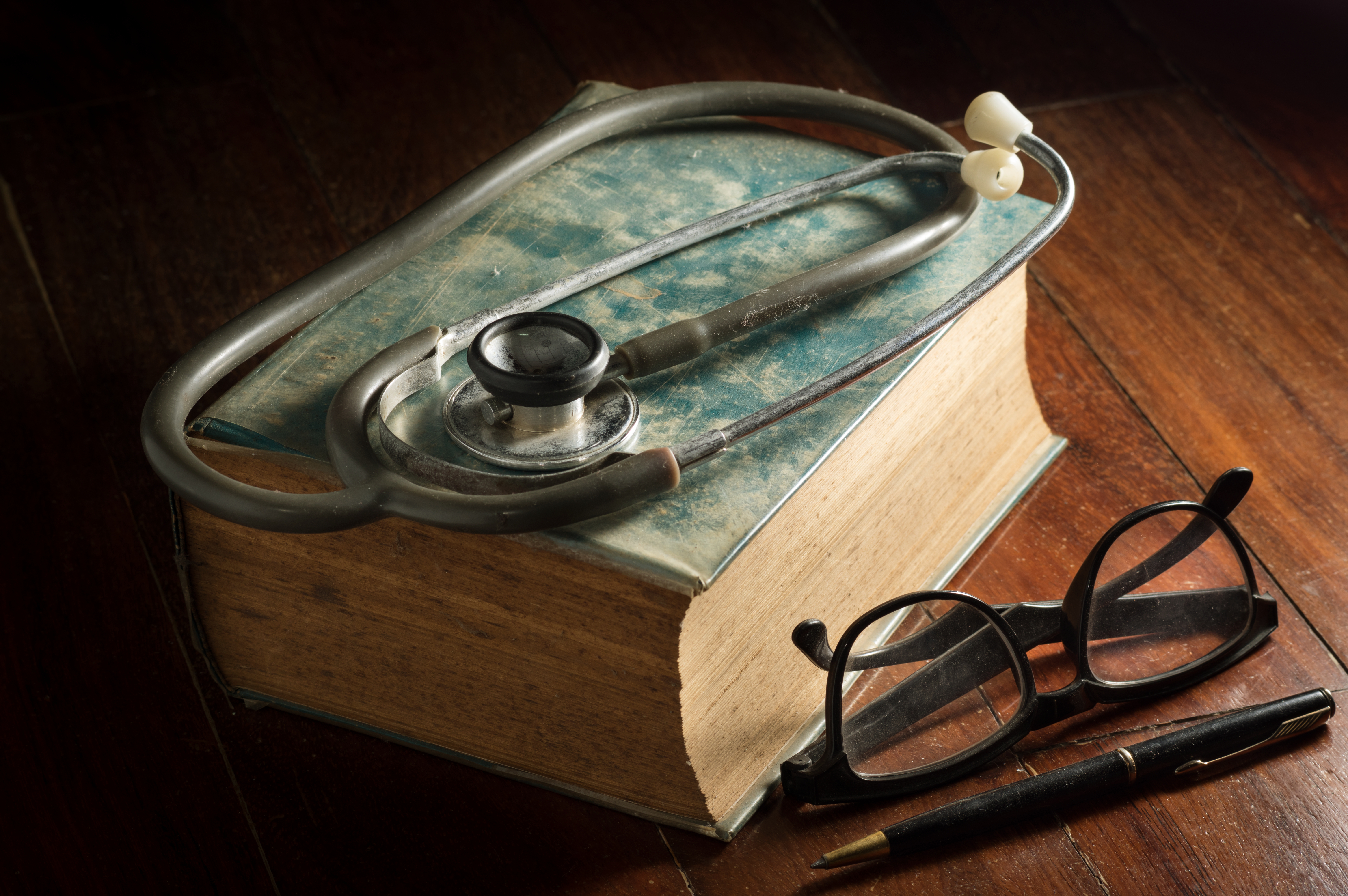 Stethoscope with eyeglasses,pen and antique book.