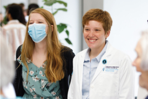 Two women, one wearing a mask, one wearing a white doctor's quote.