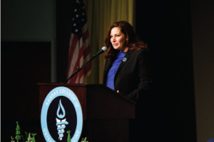 Dr. Tiffany Masson stands at podium in black suit with blue shirt.