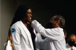 Man in white coat puts white coat on a young woman.