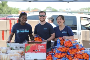 Two women and a man stand in front of boxes of produce.