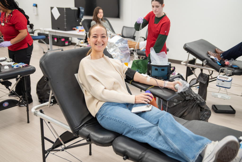 A student donates blood while smiling for the camera.