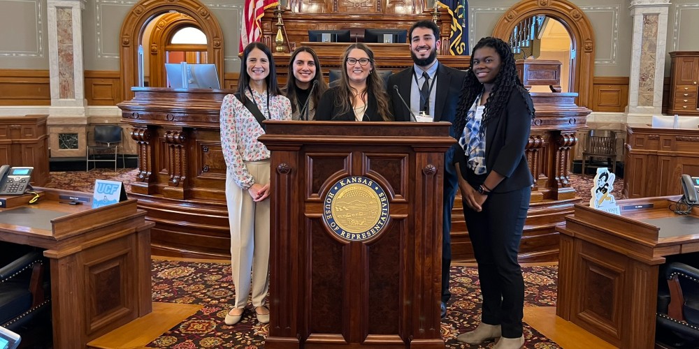 Student doctors and Dr. Carrick pause for a photo opportunity, taking in the view from the House of Representatives podium in the Kansas Statehouse.