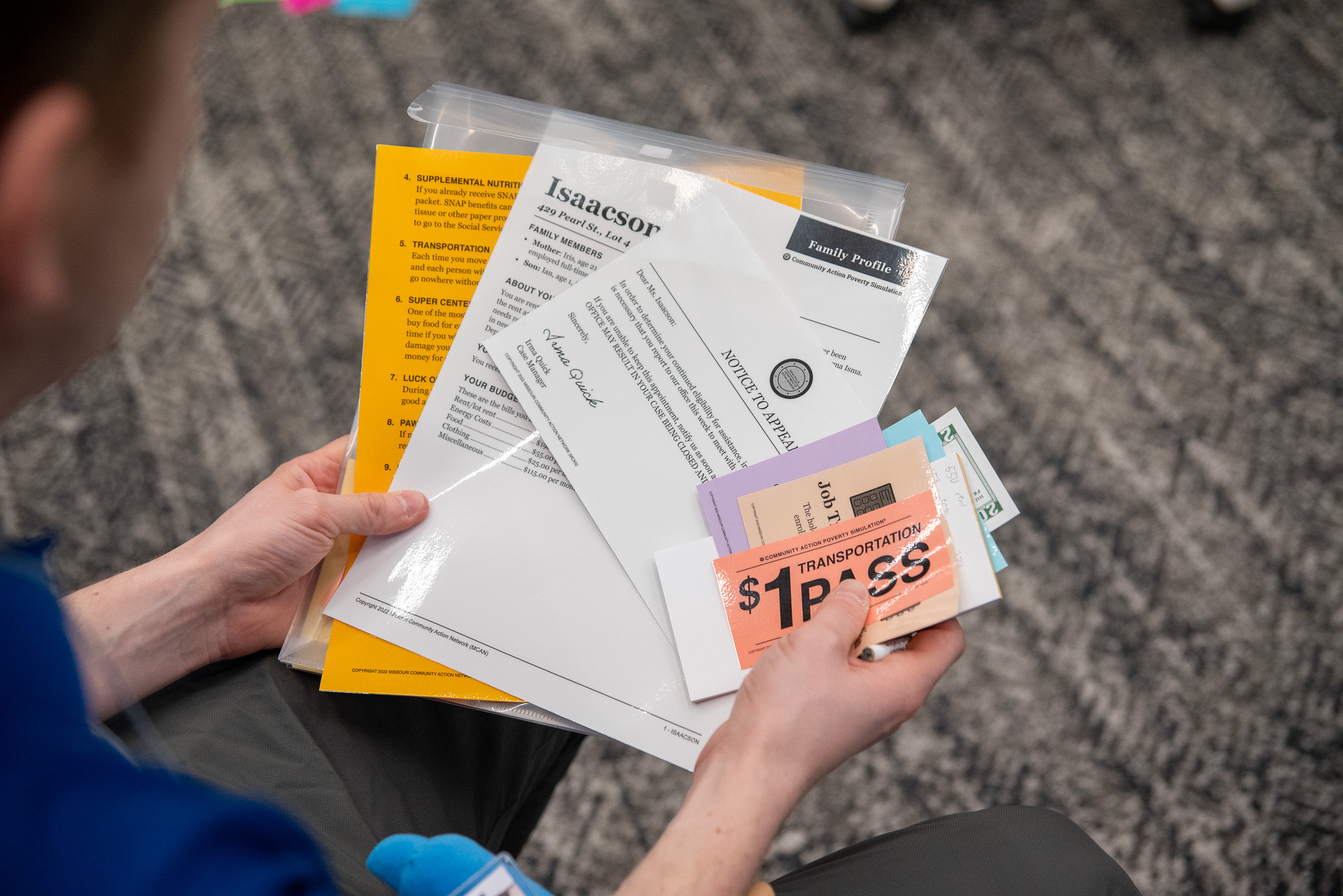 A student doctor holds the packet of information they are given to begin a poverty simulation, which includes items such as character details, transportation passes, money, etc.