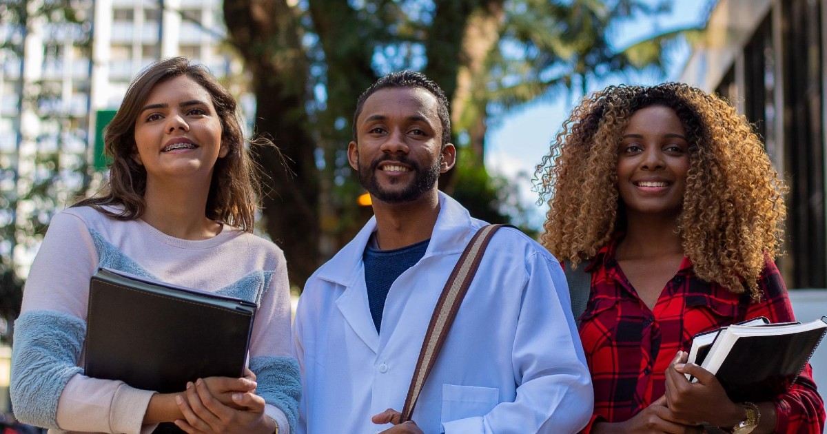 Three people holding books and documents smile at something off-camera.