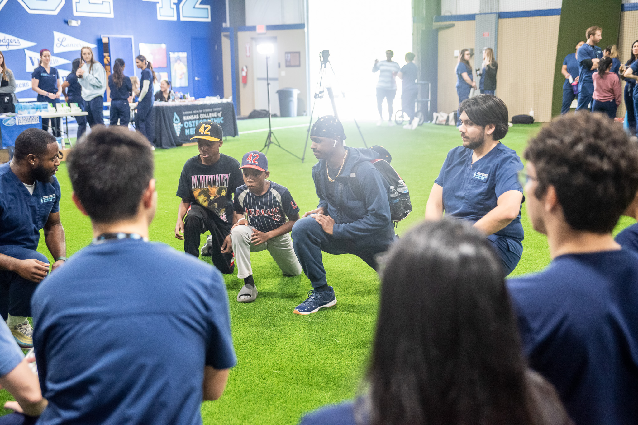 KansasCOM students kneel in a circle on an indoor field during the DO Day of Service.