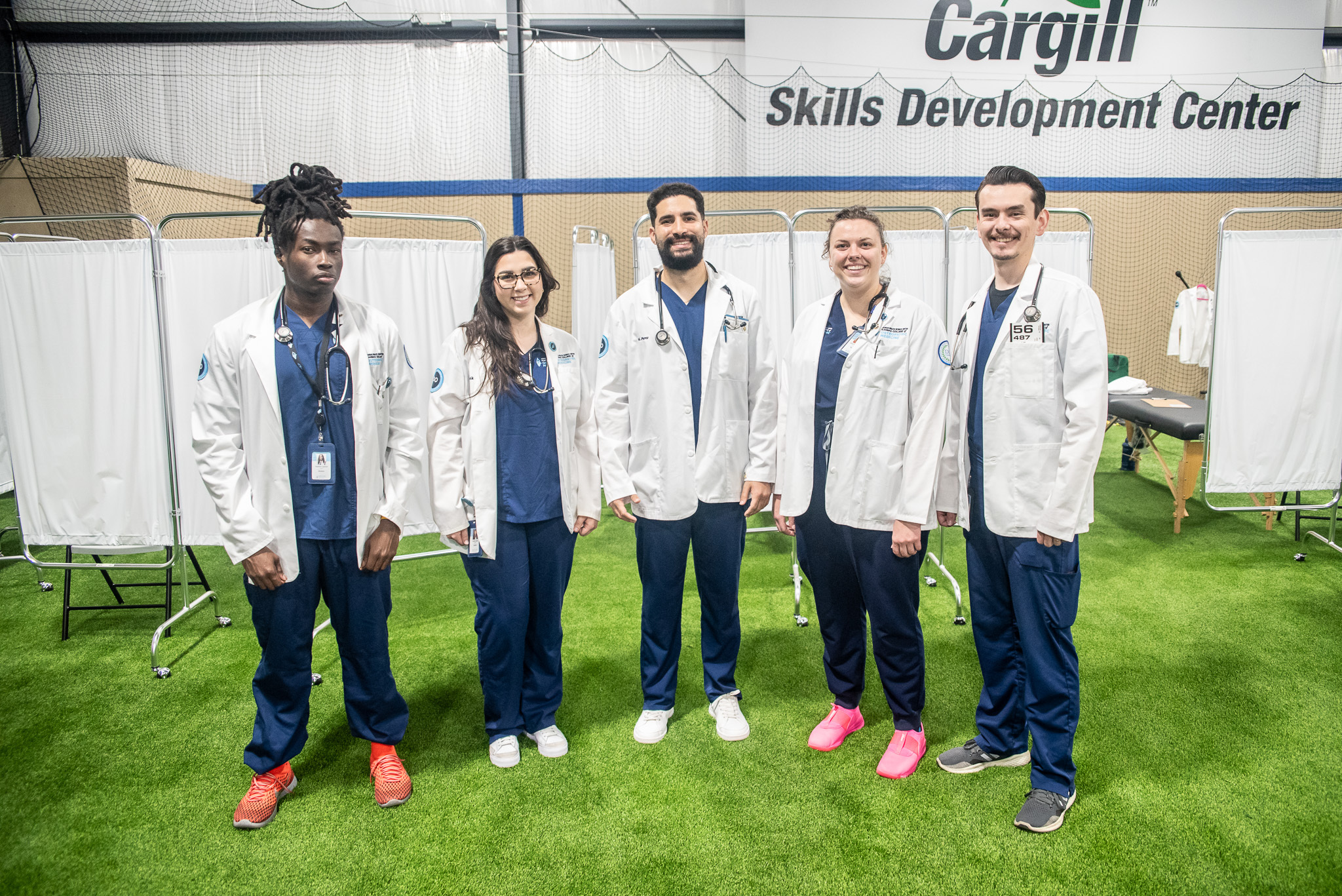 Five medical students wearing lab coats pose side by side during KansasCOM's DO Day of Service.