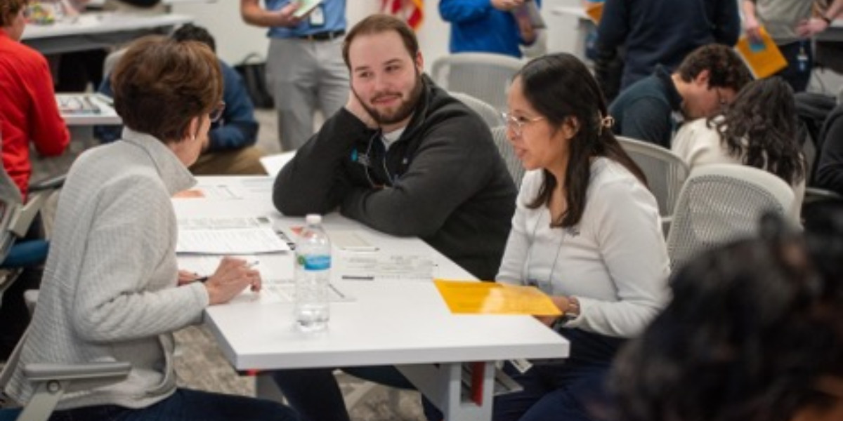 A group of young people sit around a community table chatting.