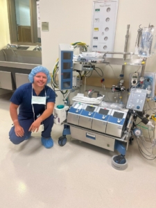 Man in surgical gear kneels my medical machine.